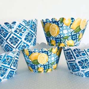 May include: A collection of decorative cupcake liners. Some liners feature a blue and white tile pattern, while others showcase lemons and green leaves against a blue and white background. The liners have a scalloped edge.
