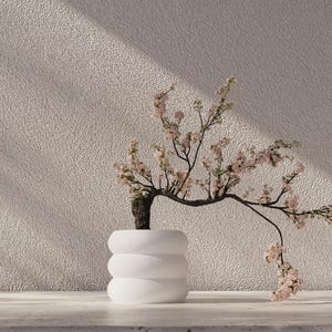 Puede incluir: Un macetero de cerámica blanca de tres niveles, con un delicado bonsái con flores rosas. El árbol se coloca contra una pared beige texturizada.