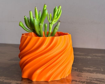 May include: A bright orange, 3D printed planter with a swirling design. A small green succulent plant is growing inside the planter.
