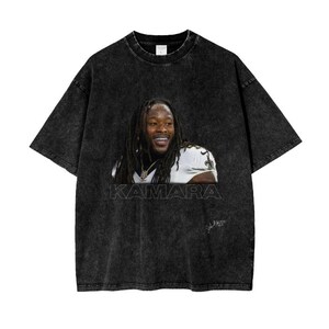 Peut inclure: T-shirt vintage noir à l'aspect délavé avec une photo d'Alvin Kamara, joueur de football américain des Saints de la Nouvelle-Orléans, avec le texte "KAMARA" imprimé sous l'image.