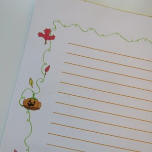 May include: White lined paper with a decorative border featuring a green vine with red and yellow leaves, and a jack-o'-lantern. The paper has a fall or Halloween theme.