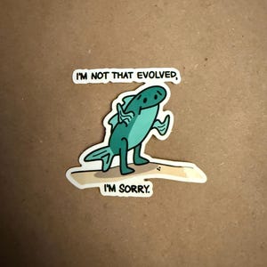 May include: A sticker with a cartoon fish with a sad expression. The fish is walking on a beach and says "I'm not that evolved, I'm sorry."