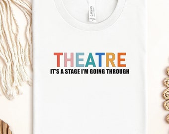 May include: White t-shirt with the text "THEATRE" in rainbow colors and the text "It's a stage I'm going through" in black.