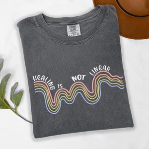 May include: A dark gray t-shirt with a rainbow graphic and the text "Healing is not linear".
