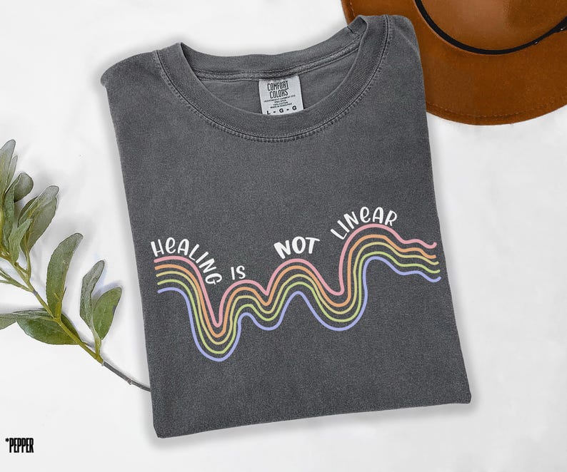 May include: A dark gray t-shirt with a rainbow graphic and the text "Healing is not linear".