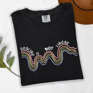 May include: Black t-shirt with a rainbow graphic and the text "Healing is not linear".