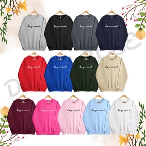 Op de afbeelding: Een set van 12 sweatshirts in verschillende kleuren, elk met de tekst "boy mom" in witte letters. De sweatshirts zijn allemaal met ronde hals en lange mouwen.