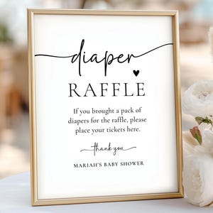 Może przedstawiać: Oprawiony znak z napisem "diaper RAFFLE" czarnym skryptem. Znak zawiera instrukcje dotyczące loterii na baby shower oraz tekst "MARIAH'S BABY SHOWER". Rama jest złota, a tło białe.