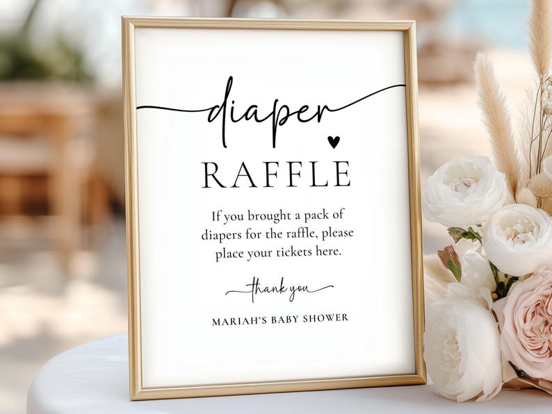 Może przedstawiać: Oprawiony znak z napisem "diaper RAFFLE" czarnym skryptem. Znak zawiera instrukcje dotyczące loterii na baby shower oraz tekst "MARIAH'S BABY SHOWER". Rama jest złota, a tło białe.