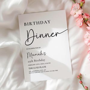 Könnte beinhalten: Eine weiße Einladungskarte mit schwarzem Text, der "GEBURTSTAG Abendessen" und Details für Mariahs 25. Geburtstag lautet. Die Karte liegt auf einem weißen Stoff mit rosa Blüten.