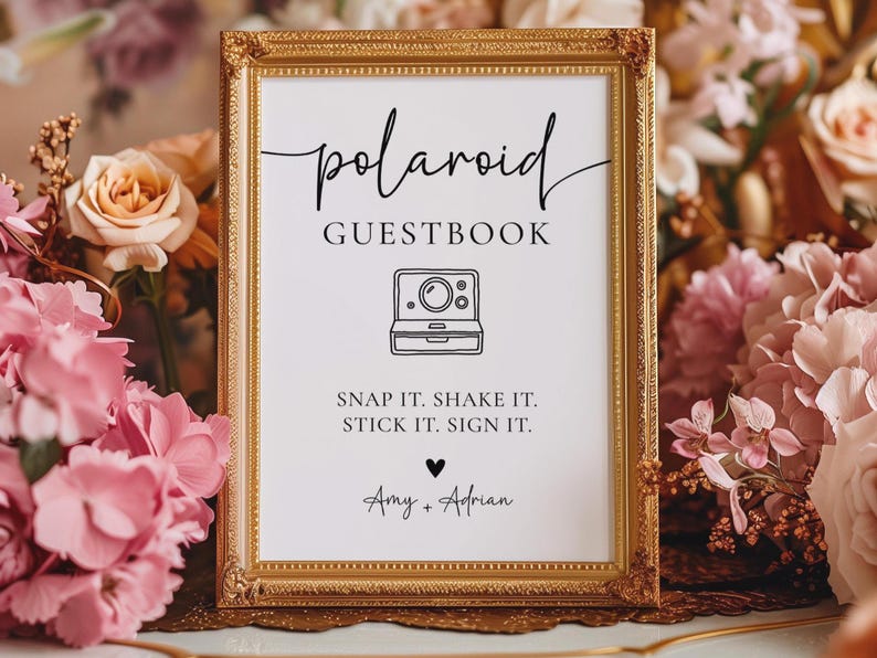 K&ouml;nnte beinhalten: Ein gerahmtes Schild mit goldenem Rand zeigt "polaroid GUESTBOOK" in Schreibschrift. Eine Strichzeichnung einer Vintage-Kamera ist abgebildet. Der Text "SNAP IT. SHAKE IT. STICK IT. SIGN IT." steht darunter, mit den Namen "Amy + Adrian".