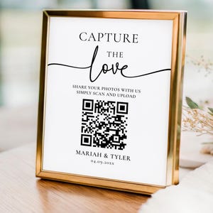 May include: A framed sign with the words "CAPTURE the love" in elegant script. Below, it reads "SHARE YOUR PHOTOS WITH US SIMPLY SCAN AND UPLOAD" with a QR code. The sign is in a gold frame, perfect for a wedding.
