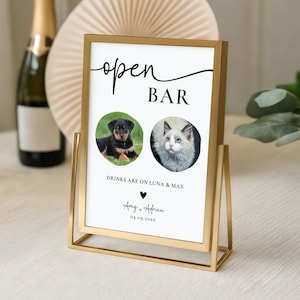 May include: Gold metal framed sign with the words "open BAR" in black script. The sign features two circular photos, one of a puppy and one of a cat. The text "DRINKS ARE ON LUNA & MAX" is below the photos, with names and a date at the bottom.