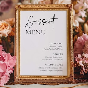 May include: A framed dessert menu with gold trim, featuring the word "Dessert" in elegant script. The menu lists cupcake, cookie, and wedding cake options, surrounded by pink and peach flowers.