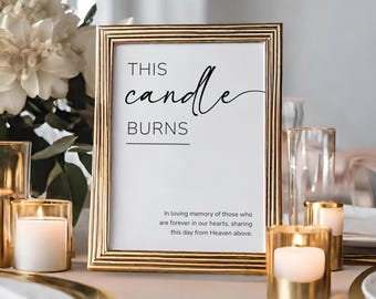 May include: A framed sign with the text "THIS candle BURNS" in elegant script. The gold frame surrounds a white background with additional text below. Several lit candles in gold holders and floral arrangements are in the background.