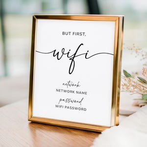 Könnte beinhalten: Ein goldgerahmtes Schild mit den Worten „But first, wifi“ in eleganter Schrift. Darunter stehen „network“, „network name“ und „password“, mit „wifi password“ am unteren Rand. Das Schild steht auf einer Holzoberfläche.