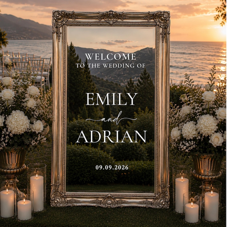 May include: A rectangular mirror with an ornate metallic gold frame featuring white text that reads: WELCOME TO THE WEDDING OF EMILY and ADRIAN 09.09.2026. The mirror reflects a landscape of trees, mountains, and a sunset over the ocean.