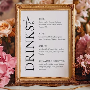 May include: A framed drinks menu with a gold ornate frame. The menu lists beer, wine, spirits, and a signature cocktail. The text is in black on a white background. The background features pink and peach flowers.