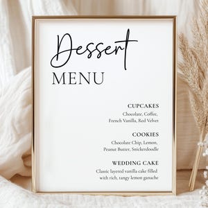 May include: A framed dessert menu with the word "Dessert" in elegant script above "MENU". The menu lists cupcake flavors like chocolate and red velvet, cookie flavors like chocolate chip and snickerdoodle, and a wedding cake description.