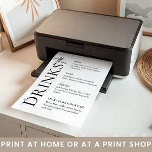 May include: A black and white printer printing a drinks menu. The menu lists beer, wine, spirits, and a signature cocktail. The text "DRINKS" is prominently displayed. The image also includes the text "PRINT AT HOME OR AT A PRINT SHOP."