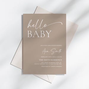 May include: A baby shower invitation with the words "hello BABY" in white script and block letters. The invitation is a light brown color and includes details such as the date, time, location, and the name "Ava Smith".