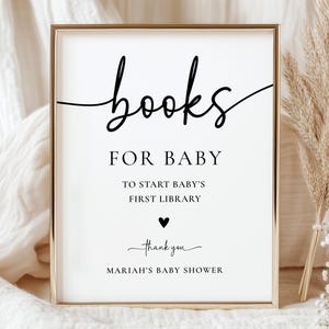 Peut inclure: Un panneau encadré avec les mots "books for baby" en écriture noire élégante. En dessous, il est écrit "to start baby's first library" avec un symbole de cœur et "thank you" suivi de "Mariah's baby shower."