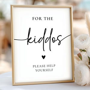 May include: A framed sign with gold trim and white background. The sign reads "FOR THE kiddos" in a stylish script font, with a small black heart below. The text "PLEASE HELP YOURSELF" is at the bottom.
