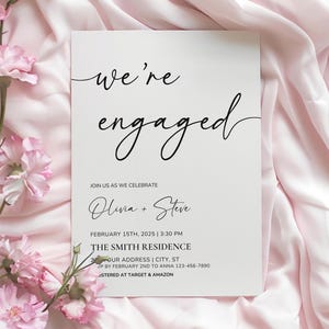 May include: A white engagement announcement card with black script that reads "we're engaged." The card includes the names Olivia and Steve, the date, time, and location of the event. Pink flowers and fabric are in the background.