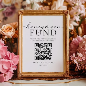 May include: A rectangular sign in an ornate gold frame featuring the text honeymoon FUND, THANK YOU FOR CELEBRATING OUR SPECIAL DAY WITH US, MARY & THOMAS, and 04.29.2027, along with a central black and white square QR code for scanning.