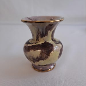 Könnte beinhalten: Eine kleine, keramische Vase mit einem marmorierten Design in Hellgelb, Rosa und Braun. Die Vase hat einen goldenen Rand und Boden.