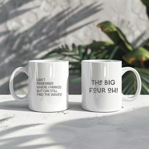 May include: Two white ceramic mugs with black text. The mug on the left says "Can't remember where I parked but can still find the waves!" The mug on the right says "The Big Four Oh!"