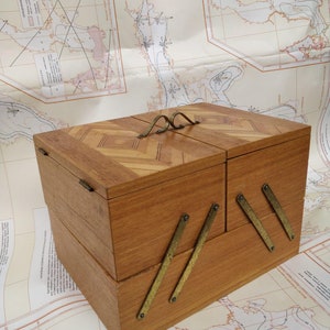 May include: A wooden box with a hinged lid and two compartments. The box has a chevron pattern on the top and brass hinges. The box is sitting on a map.