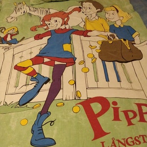 May include: A green and white bed sheet featuring a cartoon illustration of a girl with red hair and a blue dress, a boy with brown hair and a yellow shirt, and a girl with blonde hair and a blue shirt. The illustration includes a white horse, a brown purse, and gold coins. The text "Pippi L&aring;ngst" is printed in red and white on the sheet.