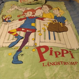 May include: A green and white bed sheet featuring a cartoon illustration of Pippi Longstocking, a girl with red hair and a blue dress, standing on a fence with a horse and two other children. The text "Pippi L&aring;ngstrump" is printed in red and white on the sheet.