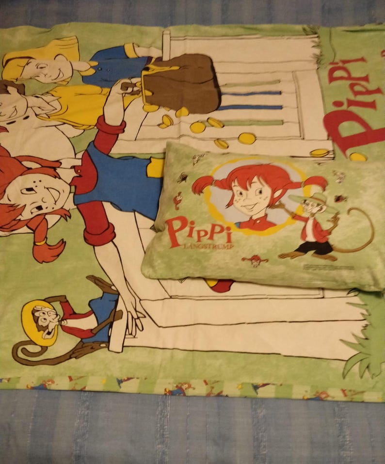 May include: A green and white bedspread featuring a cartoon image of Pippi Longstocking and her monkey, Mr Nilsson. The bedspread includes a pillow with a similar image of Pippi Longstocking and Mr Nilsson.