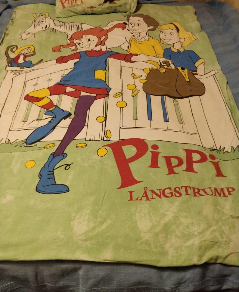 May include: A green and white bed sheet featuring a cartoon illustration of Pippi Longstocking, a girl with red hair and a blue dress, standing on a fence with a horse and two other children. The text "Pippi L&aring;ngstrump" is printed in red and white on the sheet.