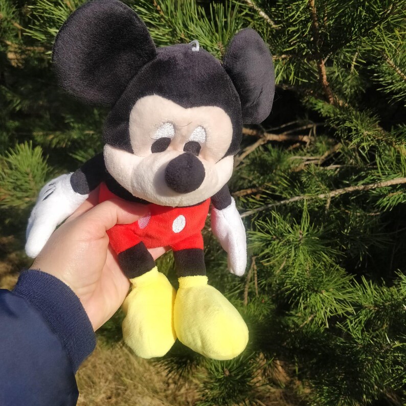 Puede incluir: Un juguete de peluche de Mickey Mouse con orejas negras, nariz negra y zapatos amarillos. El juguete lleva una camisa roja con lunares blancos.