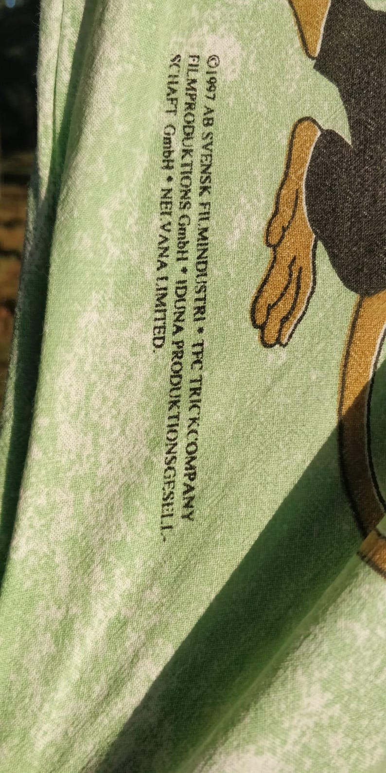 May include: A green t-shirt with a faded white print of a cartoon monkey. The text on the shirt reads "&copy;1997 AB SVENSK FILMINDUSTRI * TFC TRICKCOMPANY FILMPRODUKTIONS GmbH * IDUNA PRODUKTIONSGESELL-SCHAFT GmbH * NEI.VANA LIMITED."
