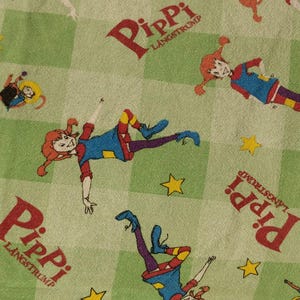 May include: Green fabric with a repeating pattern of a red-haired girl with pigtails wearing a blue dress and yellow socks. The girl is in various poses and the fabric has the text "Pippi Langstrump" repeated throughout.