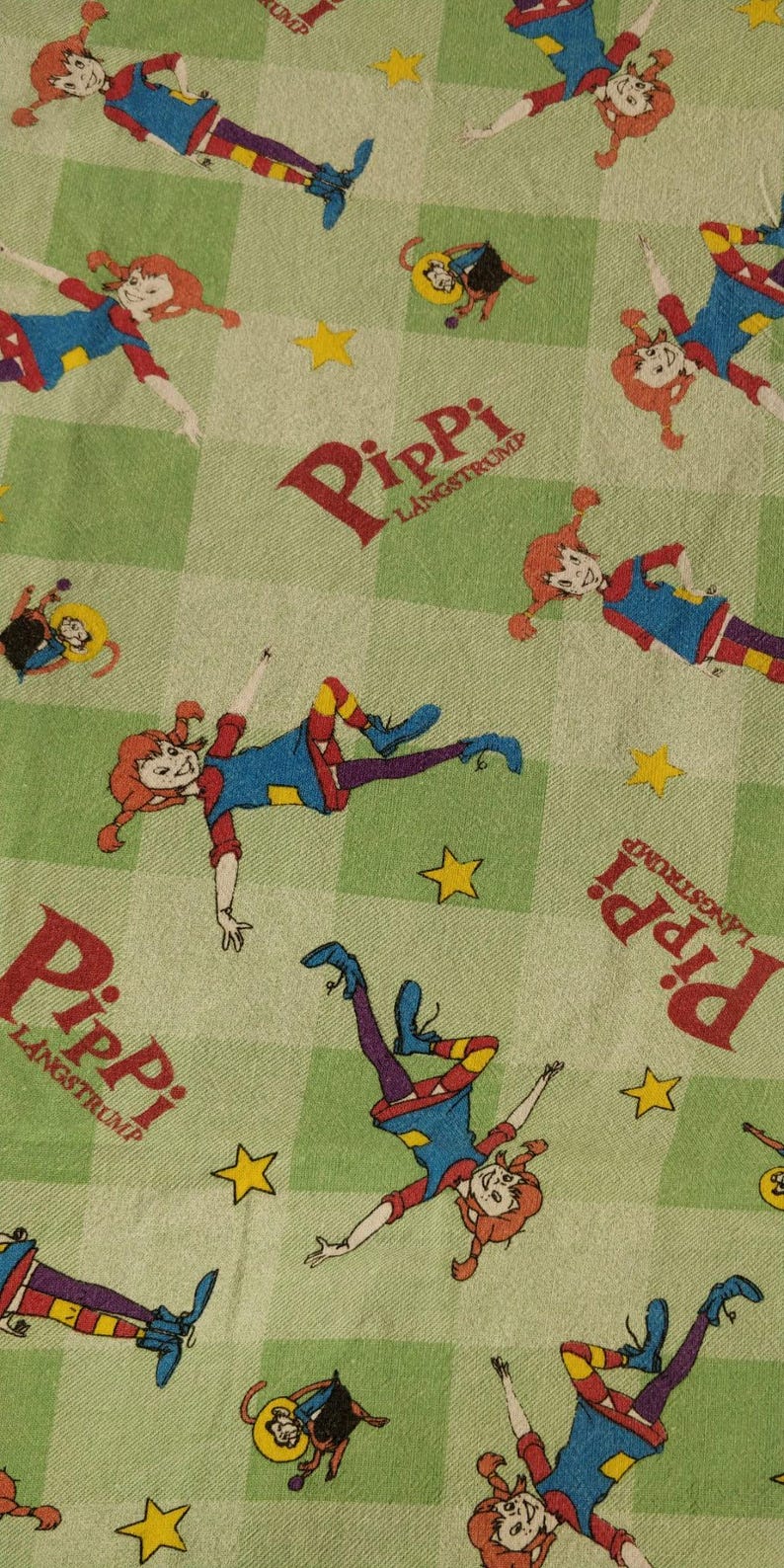 May include: Green fabric with a repeating pattern of a red-haired girl with pigtails wearing a blue dress and yellow socks. The girl is in various poses and the fabric has the text "Pippi Langstrump" repeated throughout.