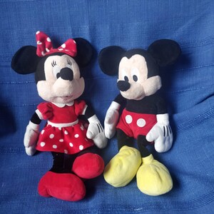 Puede incluir: Un Mickey Mouse de peluche rojo y negro y una Minnie Mouse de peluche roja y blanca. Ambos est&aacute;n de pie sobre una superficie azul.