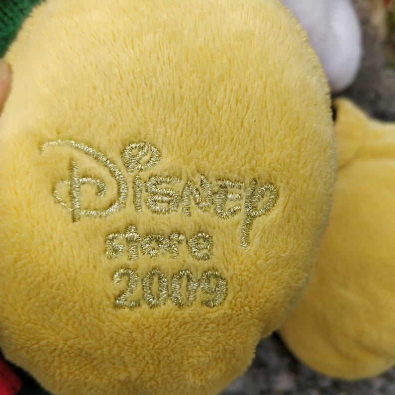 Peut inclure: Gros plan sur un jouet en peluche jaune avec le texte "Disney Store 2009" brod&eacute; en fil dor&eacute;.