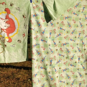 May include: Two green fabric panels with a repeating pattern of a cartoon character. The character is wearing a blue and red outfit and has a yellow star on their head. The text "Pippi" is visible on one panel.