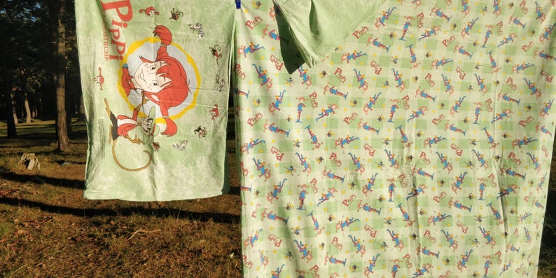 May include: Two green fabric panels with a repeating pattern of a cartoon character. The character is wearing a blue and red outfit and has a yellow star on their head. The text "Pippi" is visible on one panel.