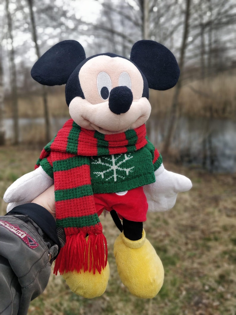 Peut inclure: Un jouet en peluche Mickey Mouse portant une &eacute;charpe ray&eacute;e verte et rouge et un pull vert avec un flocon de neige. Le jouet tient une &eacute;charpe ray&eacute;e rouge et verte.