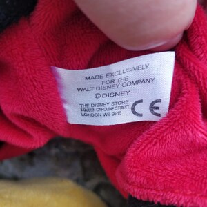 Peut inclure: &Eacute;tiquette blanche avec texte noir indiquant "Made Exclusively for the Walt Disney Company &copy;Disney The Disney Store 3 Queen Caroline Street London W6 9PE" et un marquage CE.