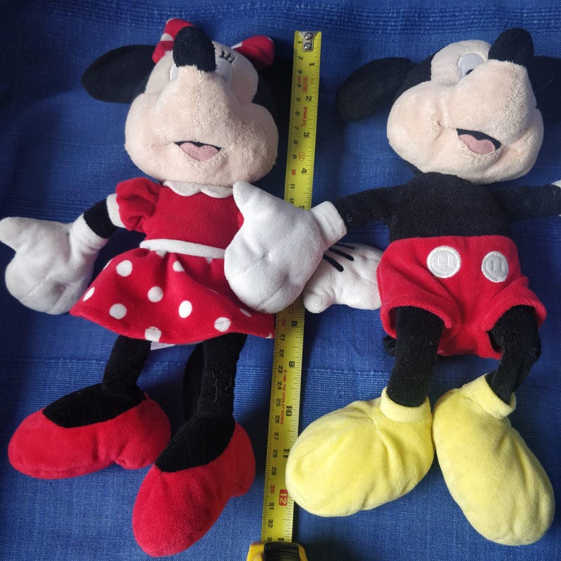 Puede incluir: Un par de peluches de Mickey Mouse y Minnie Mouse. Minnie Mouse lleva un vestido rojo con lunares blancos y un lazo rojo. Mickey Mouse lleva pantalones cortos rojos con un bot&oacute;n amarillo y zapatos negros.