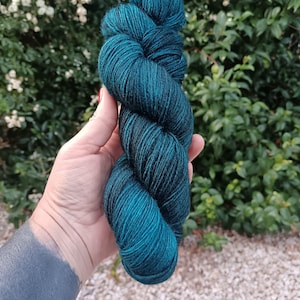 Peut inclure: Un écheveau de fil présentant une couleur sarcelle profonde et riche avec de subtiles variations de tons. Le fil a une structure torsadée à plusieurs brins avec un léger éclat, mettant en valeur un mélange vibrant de vert forêt et de turquoise.