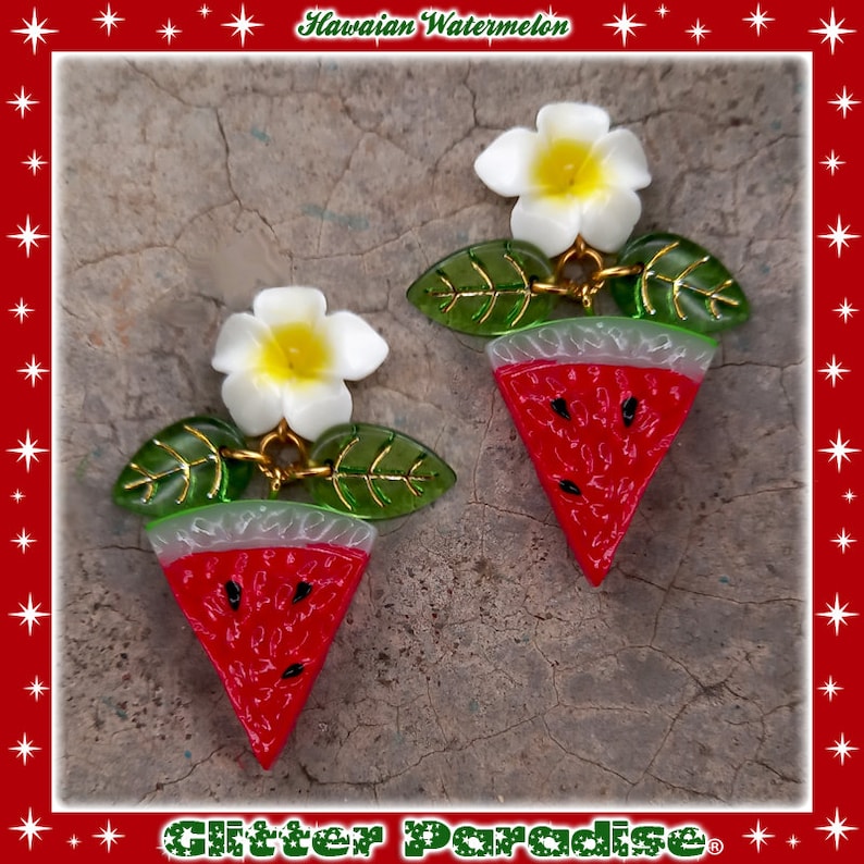 May include: A pair of watermelon slice earrings with a white plumeria flower and green leaves. The earrings are made of resin and have a glossy finish. The text "Hawaiian Watermelon" is visible at the top of the image.