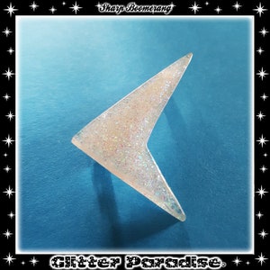 May include: A white boomerang with iridescent glitter, shaped like a sharp arrow, against a blue background. The text "Sharp Boomerang" is at the top of the image and "Glitter Paradise" is at the bottom.